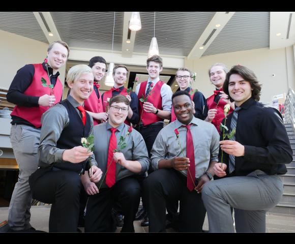 A group picture of men holding a flower wearing grey, red, and, black