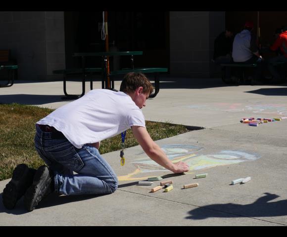 Child drawing on sidewalk with yellow and green chalk